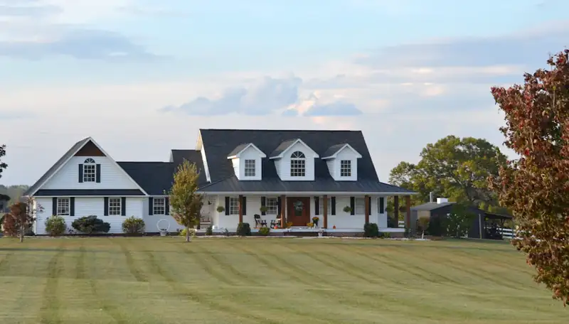 White farmhouse with a dark metal roof and wraparound porch